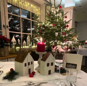 Restaurantansicht mit Weihnachtsbaum und festlich dekoriertem Tisch, beleucheteten Fenstern und Kerze